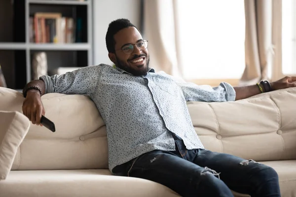 Relaxed african man hold remote control watching tv at home — 스톡 사진