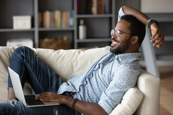 Relaxed african man resting on couch using laptop at home — Stock Photo, Image