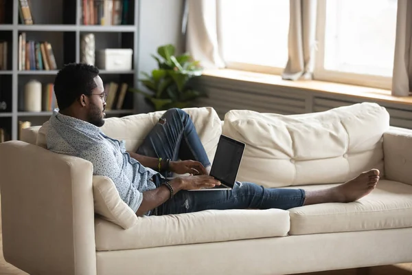 Joven afroamericano hombre usando portátil salón en sofá —  Fotos de Stock