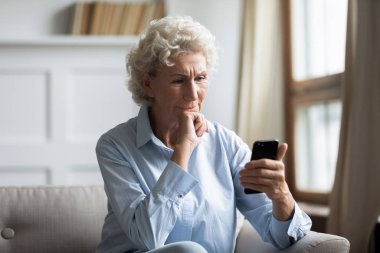 Düşünceli orta yaşlı, beyaz bir kadın elinde akıllı bir telefonla haberleri okuyor..