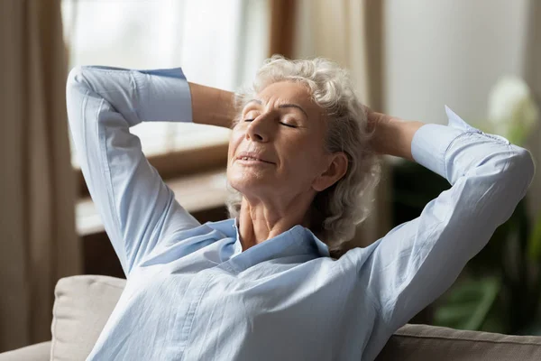 Serene volwassen vrouw ontspannen op comfortabele bank in de woonkamer. — Stockfoto