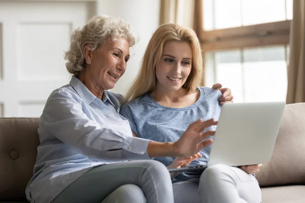 Feliz joven mujer enseñando aplicaciones de uso de la madre anciana en el ordenador portátil . —  Fotos de Stock