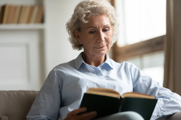 Mujer mayor pacífica leyendo interesante libro de papel bestseller . —  Fotos de Stock