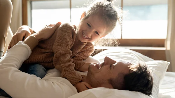 Sonriente joven padre divertirse jugando con hija en dormitorio — Foto de Stock