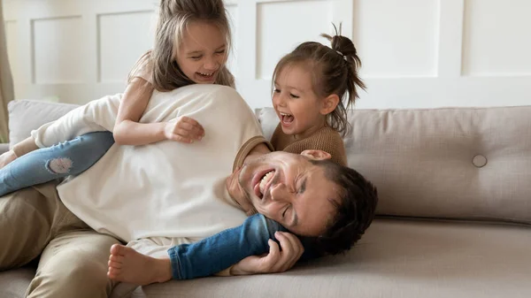 Overgelukkig jonge vader en kleine dochters spelen in de woonkamer — Stockfoto
