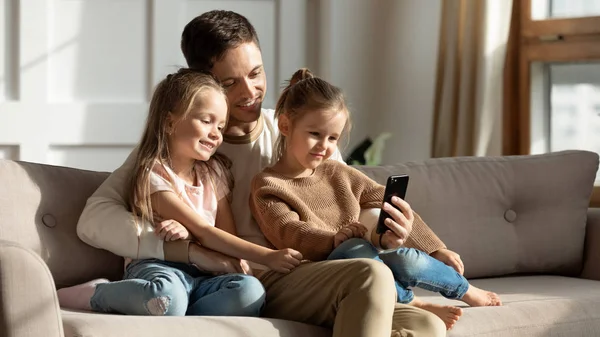 Young dad watch video on cellphone with little daughters — Stock Photo, Image