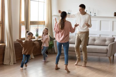 Küçük çocuklu mutlu bir aile oturma odasında dans ediyor.