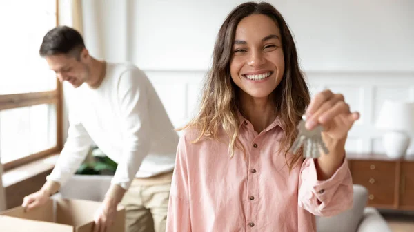 Sorridente giovane moglie mostra le chiavi che si muovono insieme con il coniuge — Foto Stock