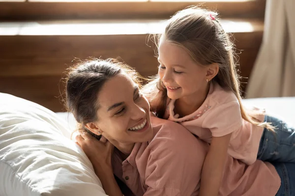 Smiling little girl relax in bedroom with young mom — Stock Photo, Image