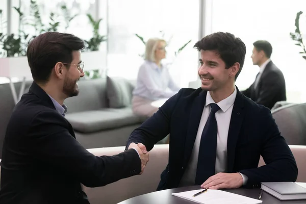 Smiling businessmen in suits shaking hands after signing agreement. — Stock Photo, Image