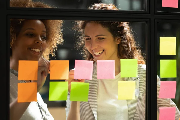 Sonrientes mujeres multirraciales escriben en coloridas notas adhesivas —  Fotos de Stock