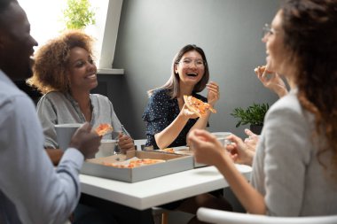 Gülümseyen çok ırklı meslektaşlar ofiste pizza yerken eğleniyor.