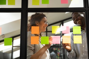 Gülümseyen çok ırklı meslektaşlar yapışkan notlar projesinde işbirliği yapıyorlar