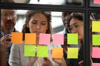Odaklanmış çok ırklı meslektaşlar renkli yapışkan notlar üzerine yazıyorlar