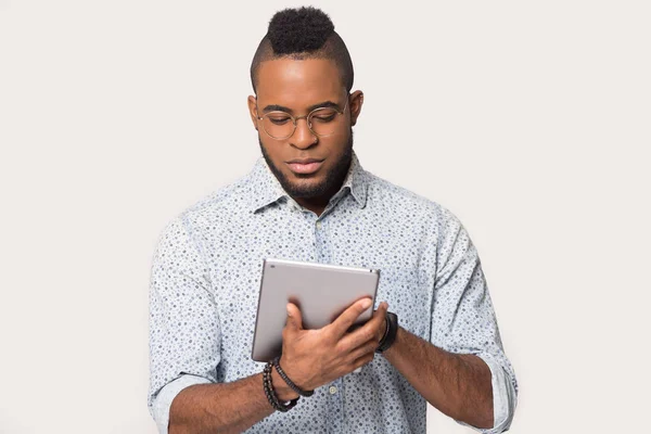 Black male in glasses isolated on grey background using tablet — Stock Photo, Image