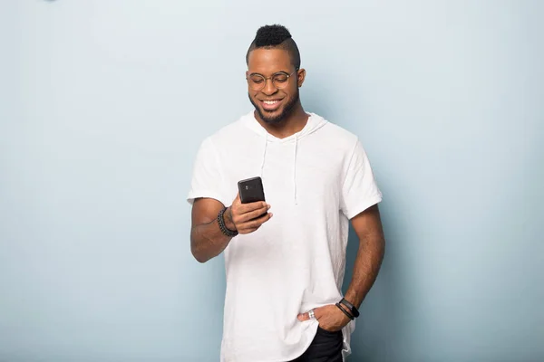 Sorrindo preto macho isolado em estúdio usando mensagens de texto de celular — Fotografia de Stock