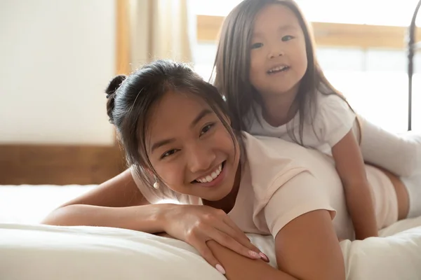 Happy Asian mother and small daughter cuddle in bed — Stock Photo, Image