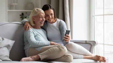 Mutlu orta yaşlı anne ve yetişkin kız akıllı telefondan selfie çekiyorlar.
