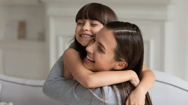 Маленькая девочка обнимает улыбающуюся молодую мать показывая любовь — стоковое фото