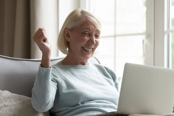 Счастливая пожилая женщина триумф читать хорошие новости на ноутбуке — стоковое фото