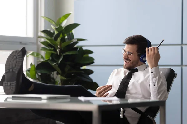 Empresário sentado no local de trabalho usando fones de ouvido ouve música desfrutar de pausa — Fotografia de Stock