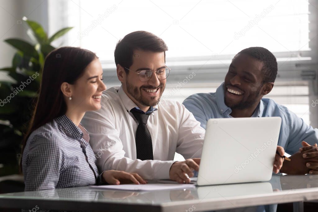 Cheery workers sitting at desk watching funny videos on laptop