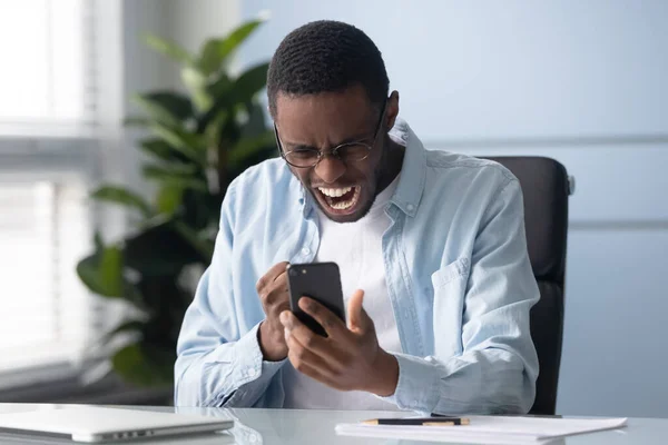 Africano homem segurando celular gritando se sente ultrajado com problemas de gadget — Fotografia de Stock