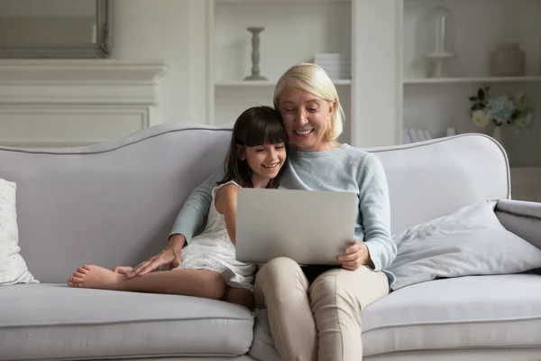 Счастливая бабушка и маленькая внучка смотрят ноутбук дома — стоковое фото