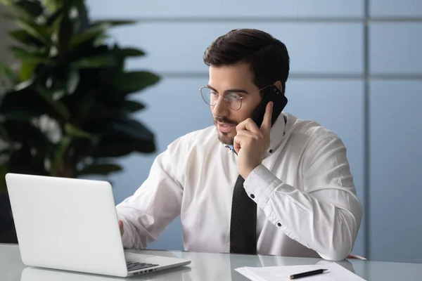 Empresário olha para tela do computador falando por telefone consultar cliente — Fotografia de Stock