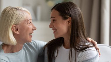 Mutlu yetişkin anne ve yetişkin kız evde konuşuyor.