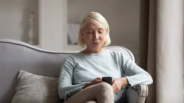 Женщина средних лет сидит на диване с помощью мобильного телефона — стоковое фото