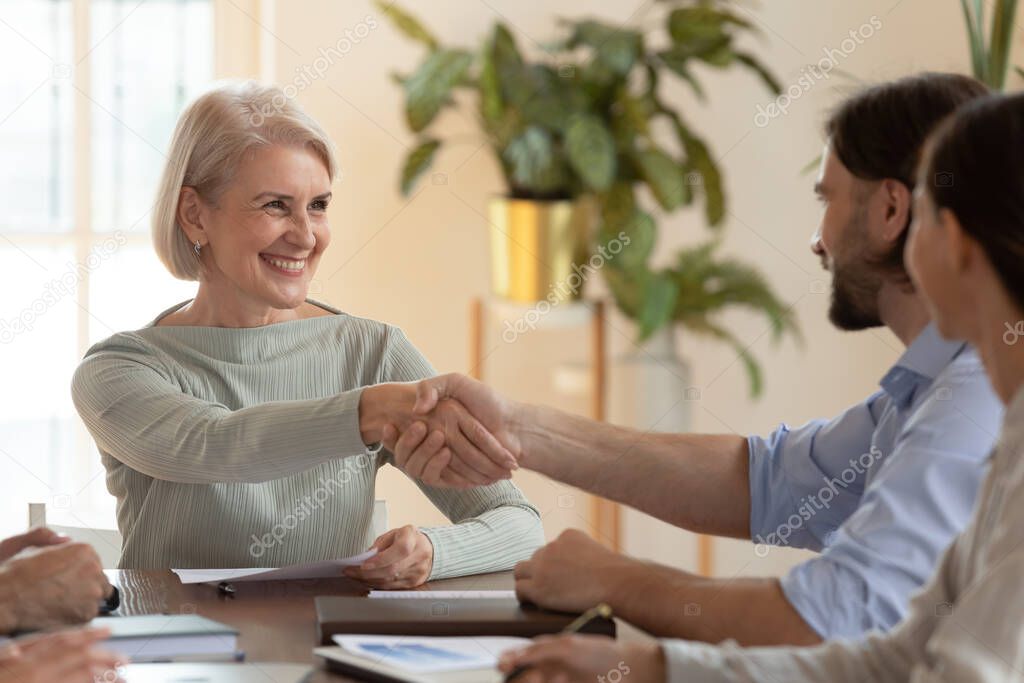 Smiling middle-aged businesswoman handshake male colleague at office briefing