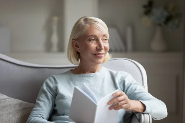 Mujer madura feliz distraída de leer libro en casa —  Fotos de Stock