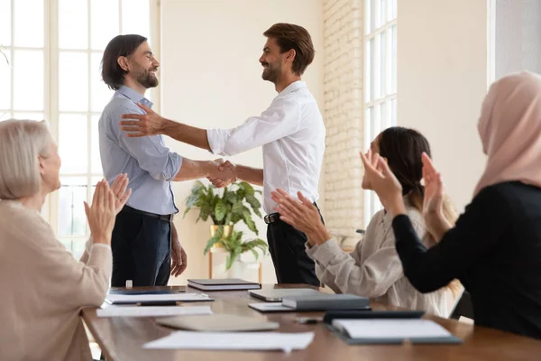 Sonriente hombre de negocios estrechan la mano de un recién llegado masculino en la reunión —  Fotos de Stock