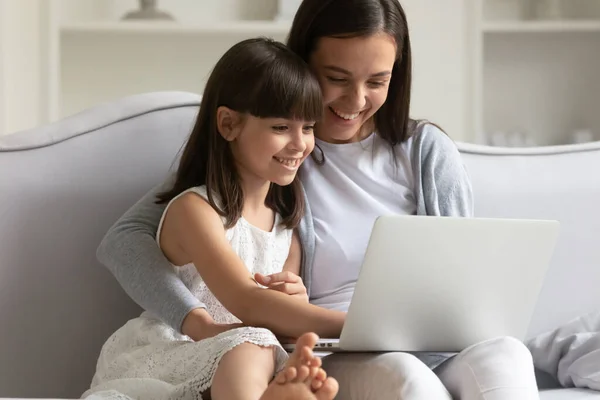 Feliz joven mamá y su hija pequeña usando el ordenador portátil en casa —  Fotos de Stock