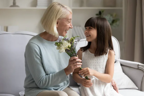 Aandachtig klein meisje begroeten opgewonden grootouder presenteren bloemen — Stockfoto