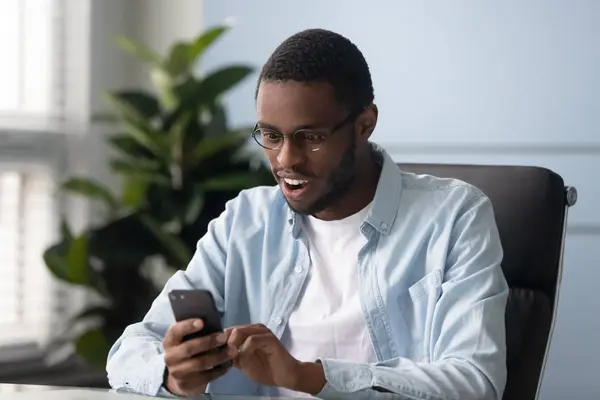 Etnia africana cara segurando smartphone ler recebeu mensagem se sente surpreso — Fotografia de Stock