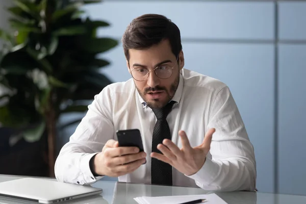 Homem de negócios irritado segurando gadget se sente irritado com smartphone quebrado — Fotografia de Stock