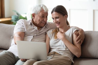 Heyecanlı yetişkin baba ve kızı dizüstü bilgisayar kullanarak gülüyorlar.