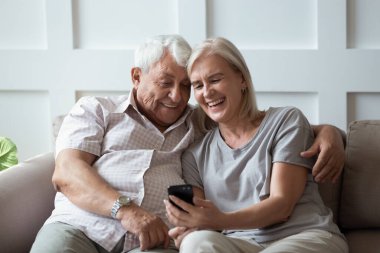 Gülümseyen olgun çift koltukta cep telefonuyla sarılır.