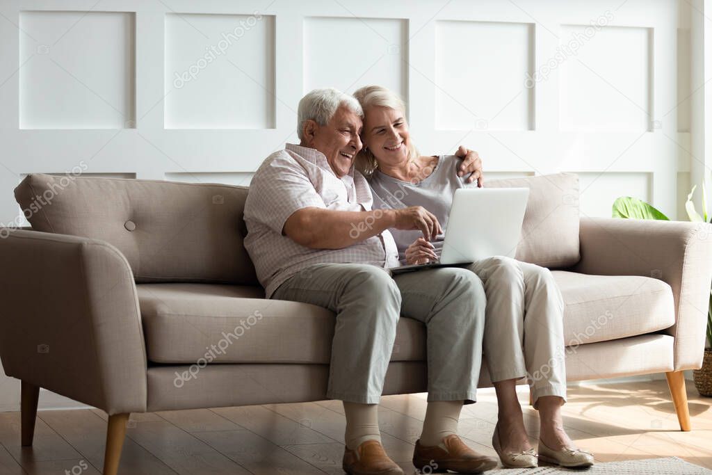 Modern mature couple have fun using laptop at home