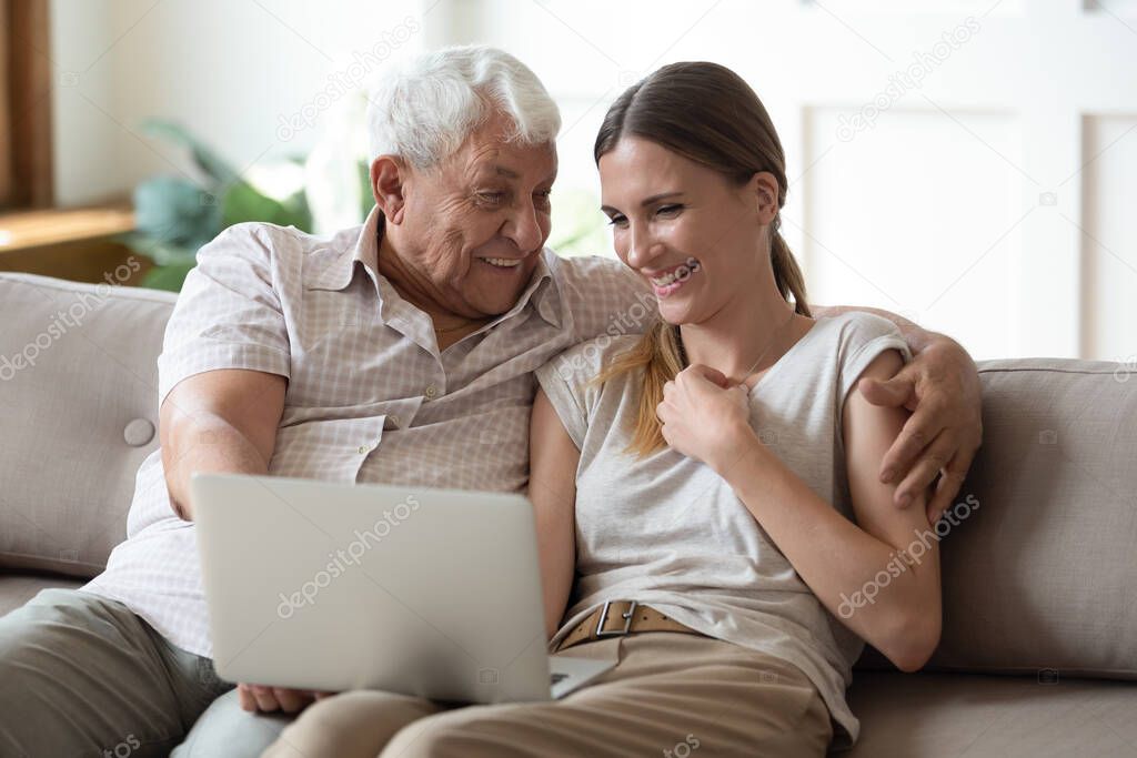 Excited mature dad and adult daughter laugh using laptop