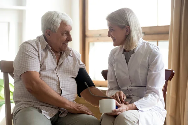 Enfermera sonriente mide la presión arterial del paciente masculino mayor — Foto de Stock