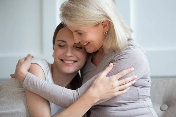 Щаслива зріла мама обіймає дорослу дочку, відпочиваючи вдома разом — стокове фото