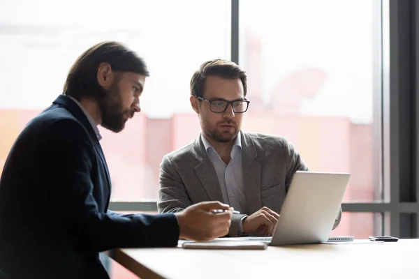 Два бизнесмена коллеги смотрят на экран ноутбука, работают вместе — стоковое фото