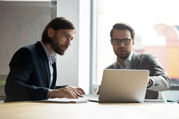 Dwóch poważnych biznesmenów omawia projekt, patrząc na ekran laptopa — Zdjęcie stockowe