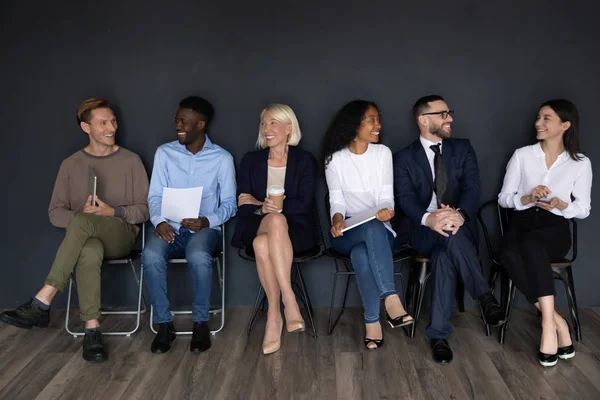 Seis empleados multiétnicos sentados en sillas cerca del fondo negro de la pared —  Fotos de Stock