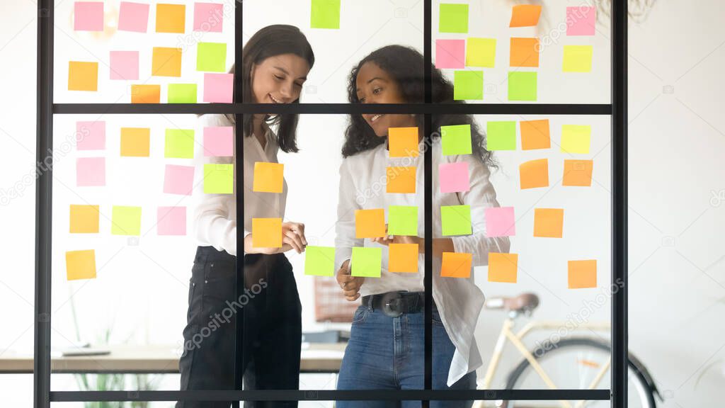 Two multiethnic affiliates create ideas writing it on sticky notes