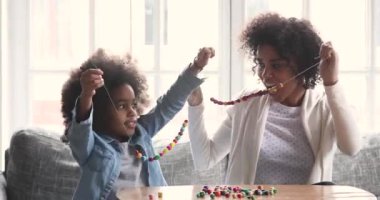 Happy african mom and child daughter making necklace giving high-five
