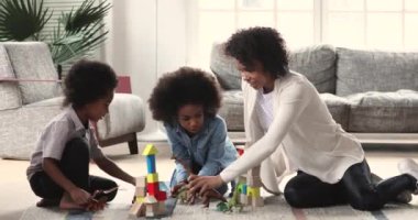 African mom babysitter playing with kids on living room floor